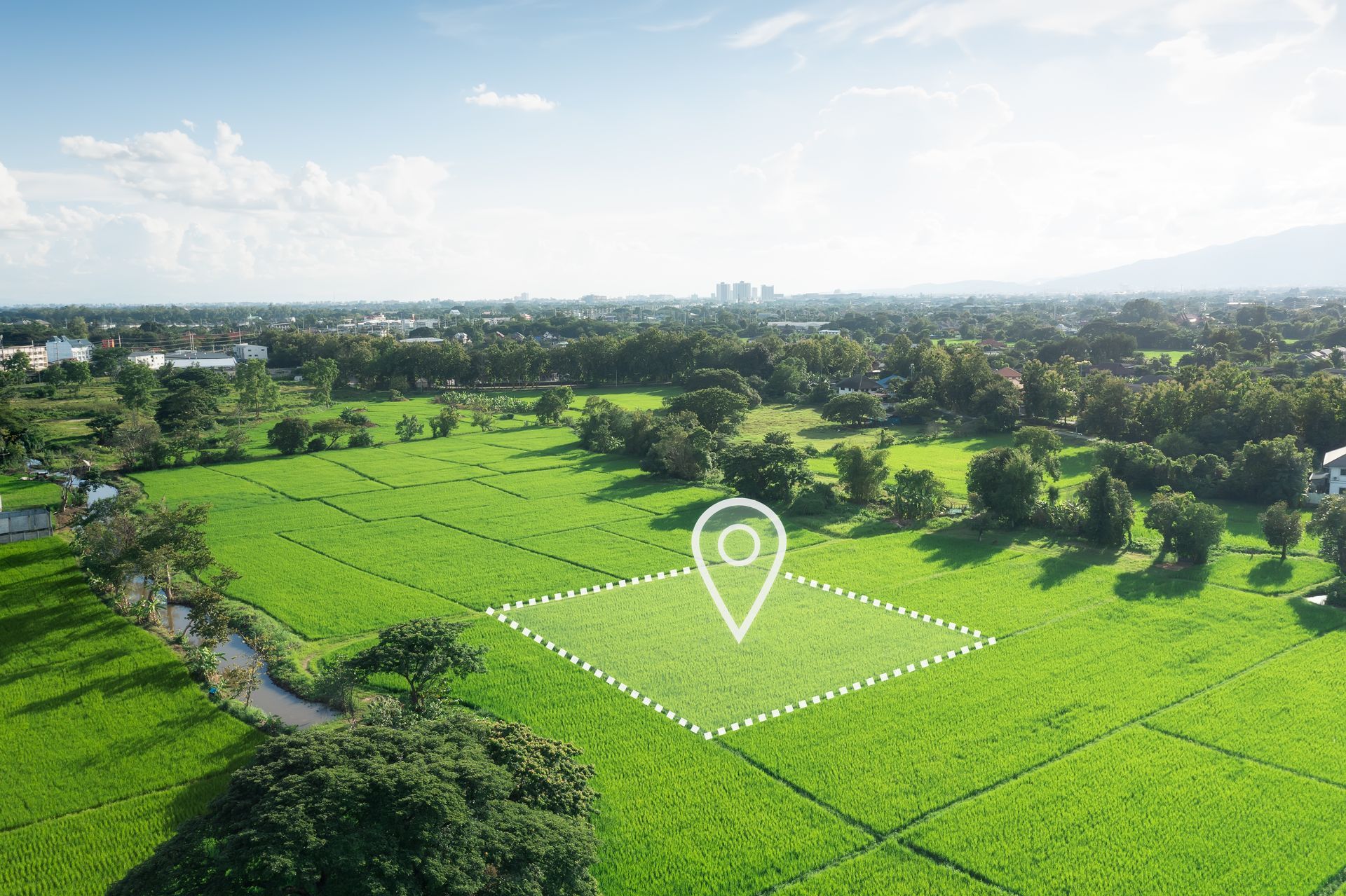 Vue aérienne de terres agricoles d'un vert éclatant, avec une épingle blanche indiquant une parcelle près des arbres et des bâtiments de la ville au loin.