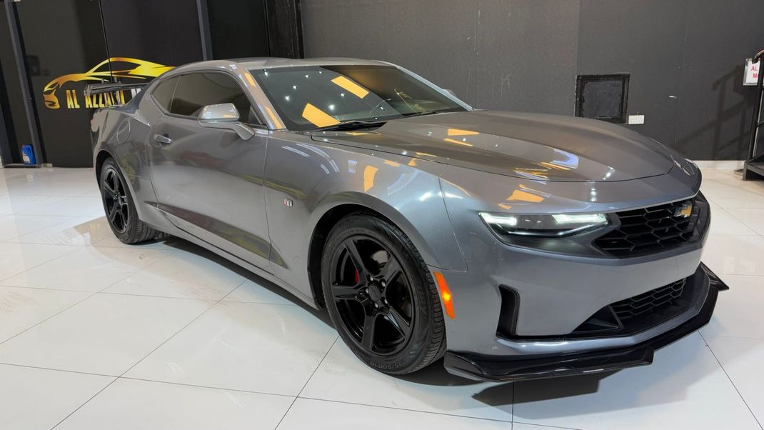 Un Chevrolet Camaro gris está estacionado en una sala de exposición.