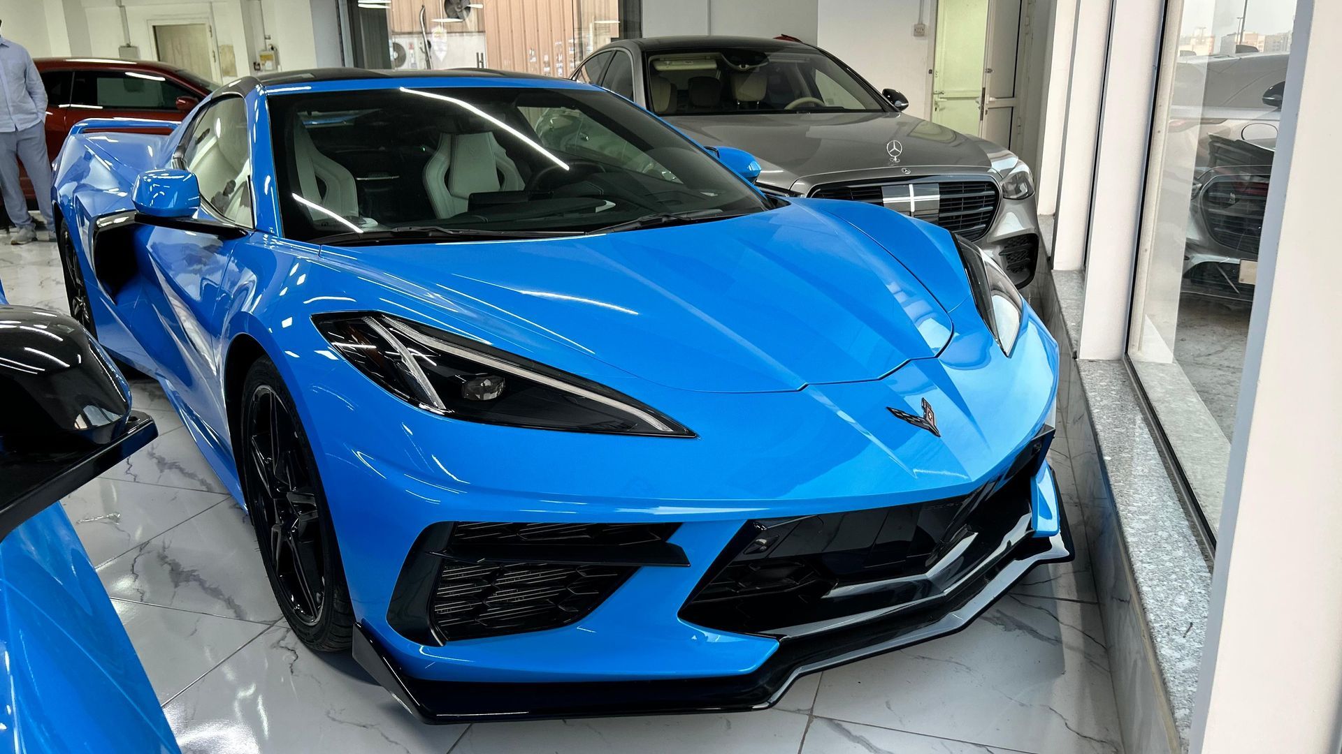 Un coche deportivo azul está aparcado en una sala de exposición al lado de un coche plateado.