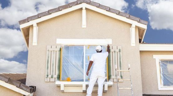 Un hombre está pintando una ventana en el costado de una casa.