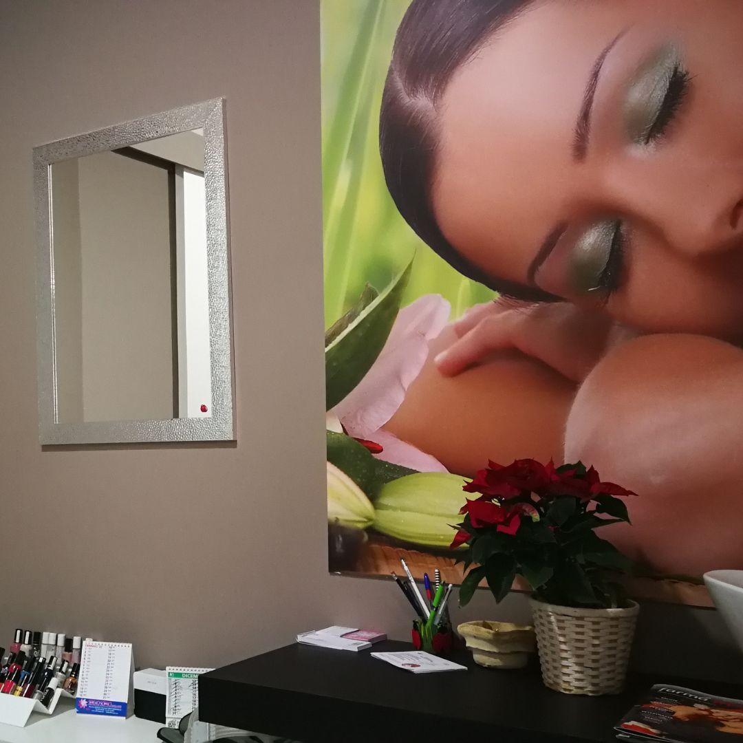 Specchio a parete accanto a una scrivania. Poster di una donna truccata sulla destra. Fiori rossi sulla scrivania.