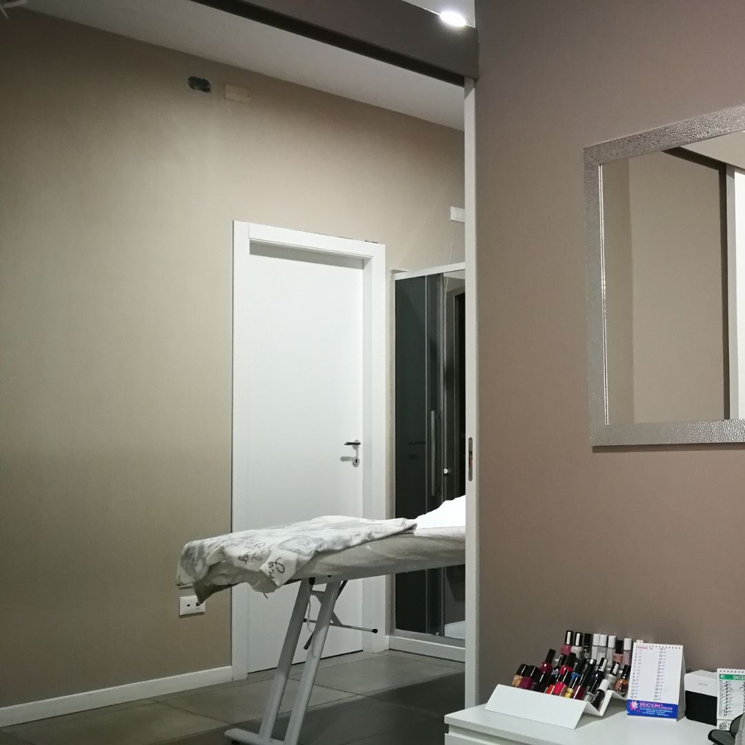 Sala trattamenti con lettino per massaggi, porta bianca, specchio e pareti beige.