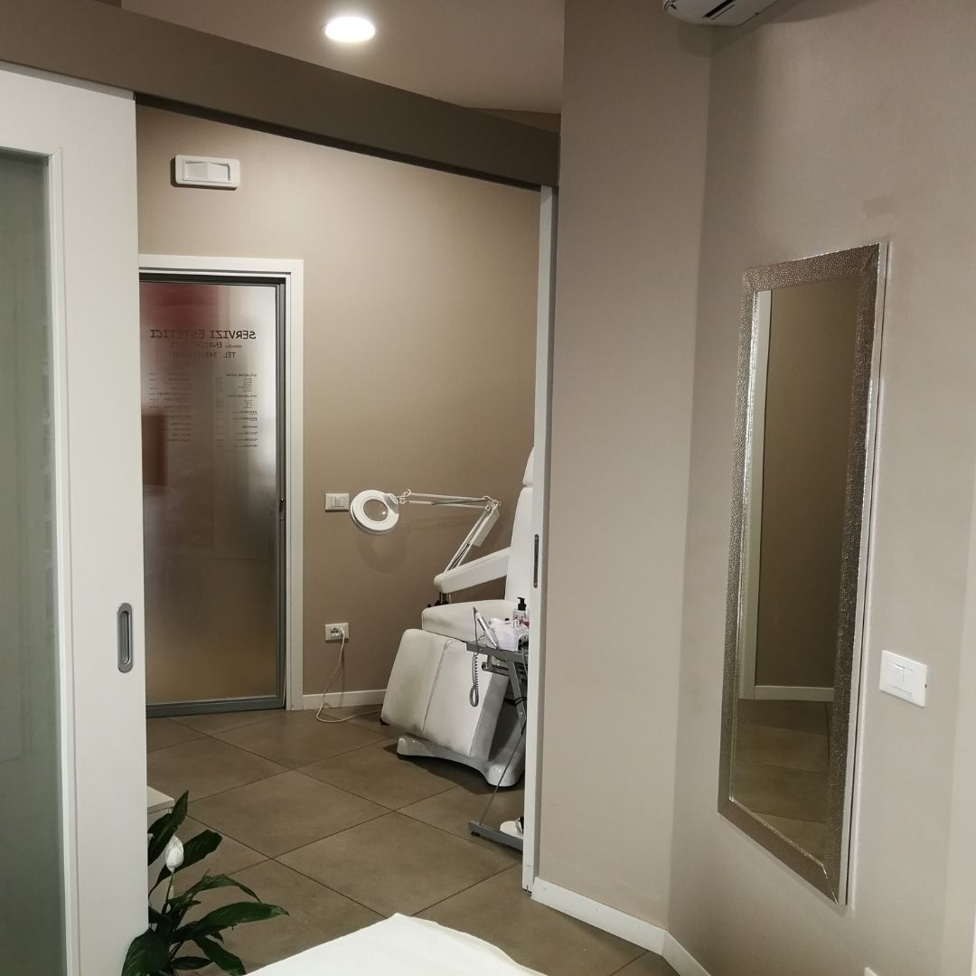 Interno di una sala per visite mediche con una porta scorrevole, attrezzature e uno specchio.