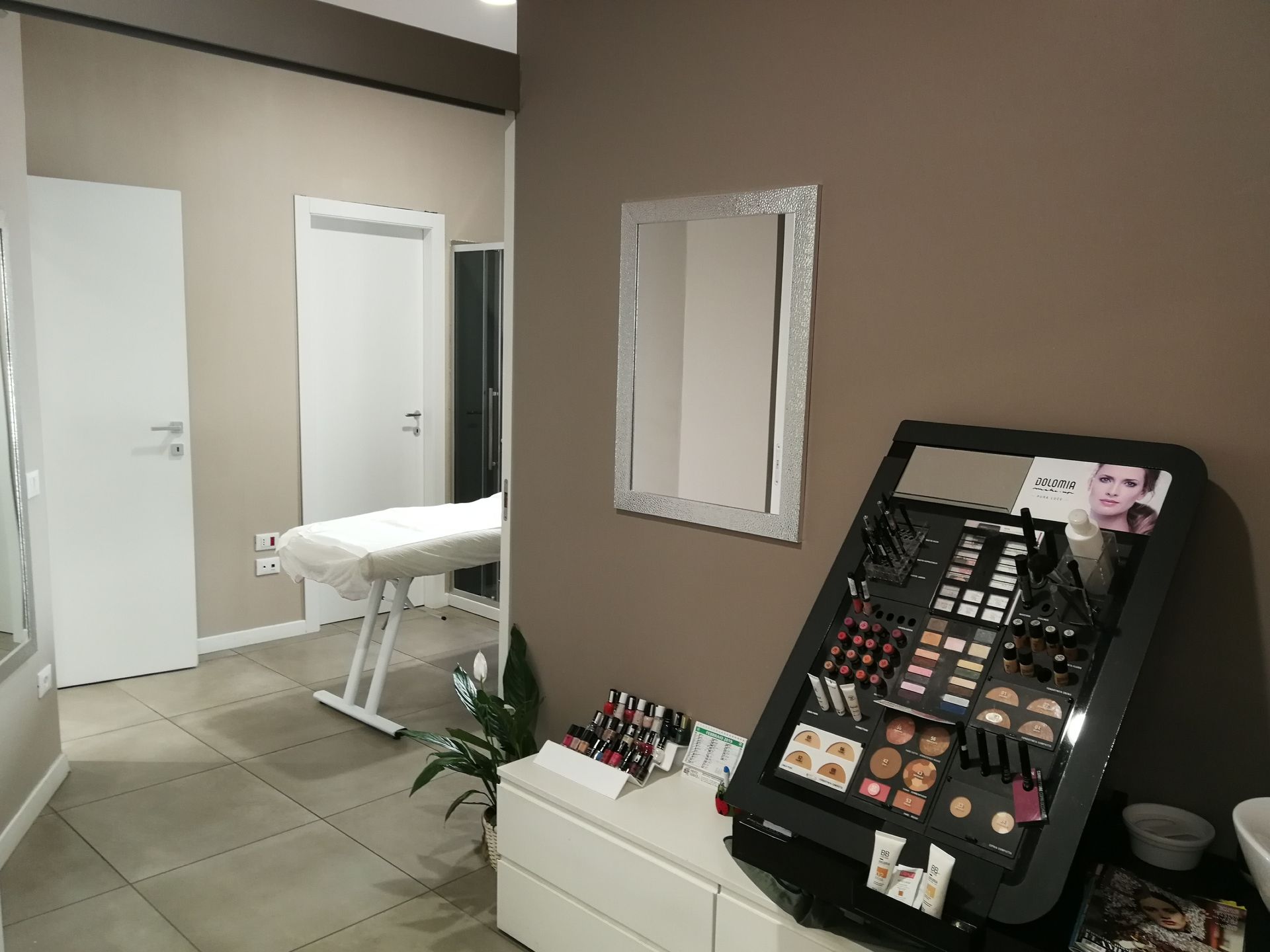 Interno di un salone di bellezza con espositore per il trucco, specchio e sala trattamenti visibili.