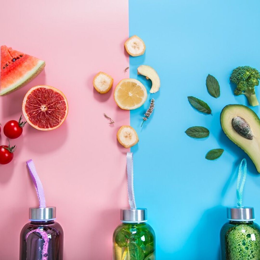 Sfondo rosa e blu con frutta e verdura colorate su bottiglie di vetro con cannucce.