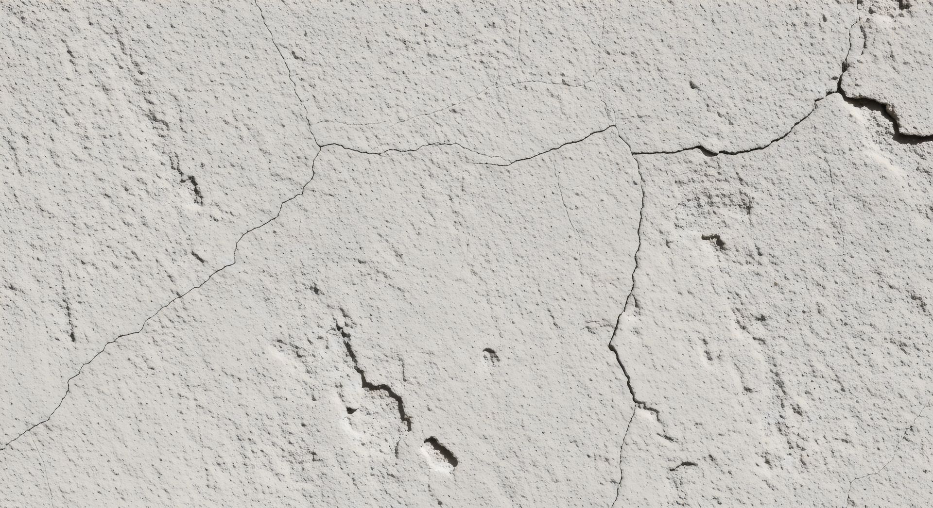 Mur en stuc blanc présentant de multiples fissures.