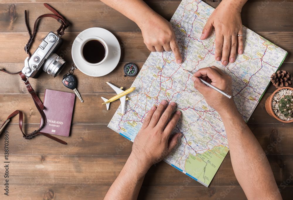 Hände planen eine Reise mit Karte, Kamera, Kaffee, Reisepass, Kompass, Flugzeug und Kaktus auf einem Holztisch.