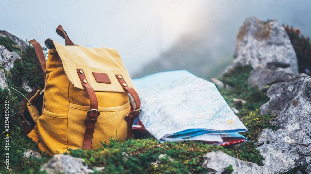Gelber Rucksack und Karte auf felsigem, grasbewachsenem Gelände in nebelverhangenen Bergen.