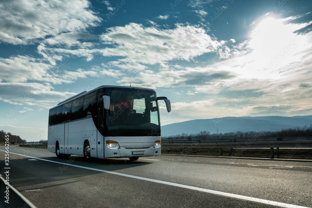 Ein weißer Bus fährt an einem sonnigen Tag auf einer Autobahn.