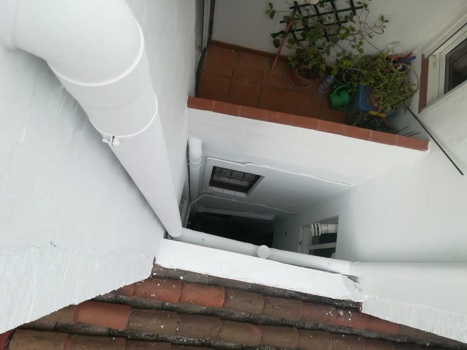 Escalera blanca empinada con escalones de ladrillo rojo y una planta en maceta en el rellano superior.