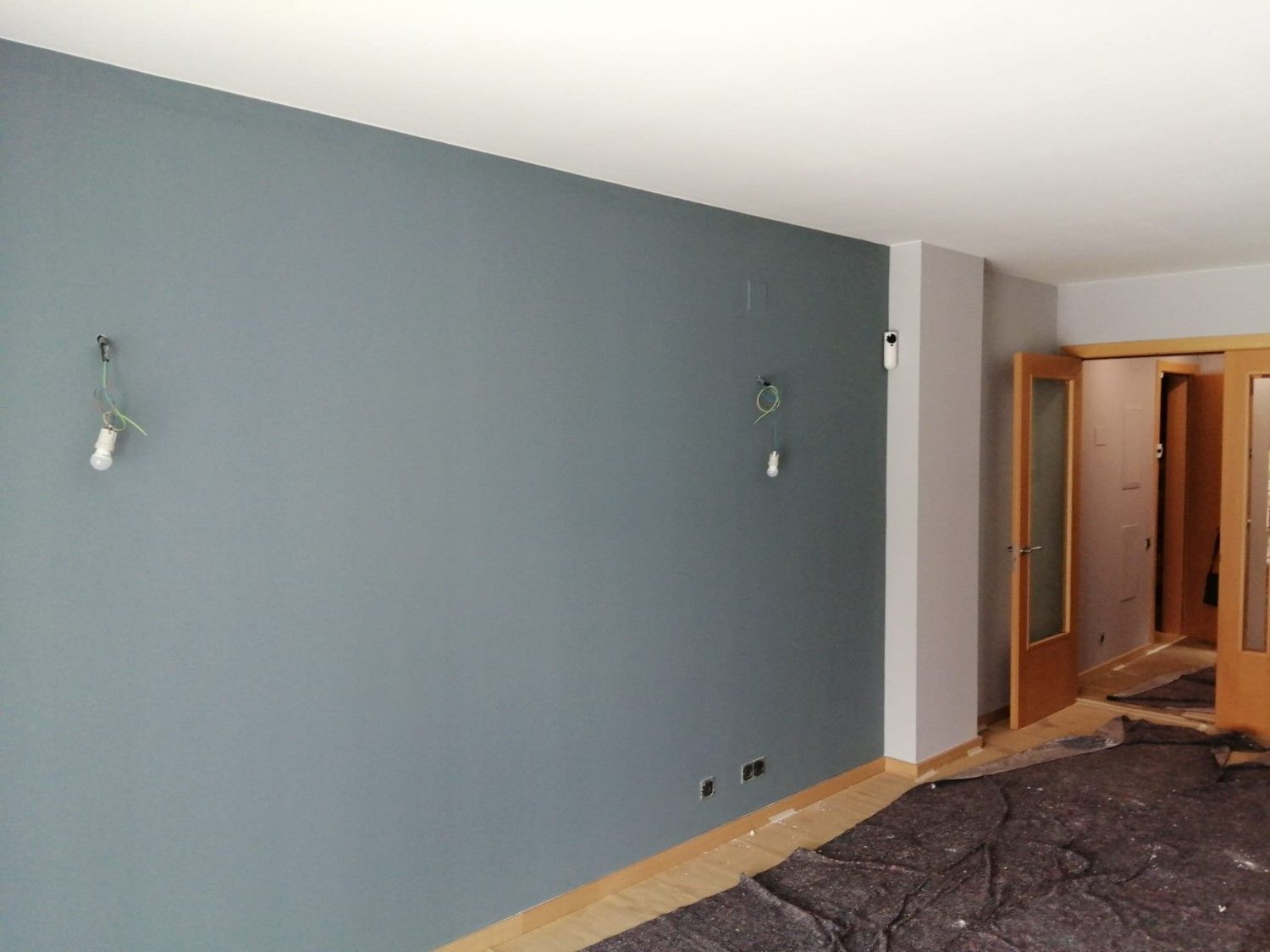 Un trabajador pinta un mural en una pared bajo un andamio, con casco blanco y guantes.