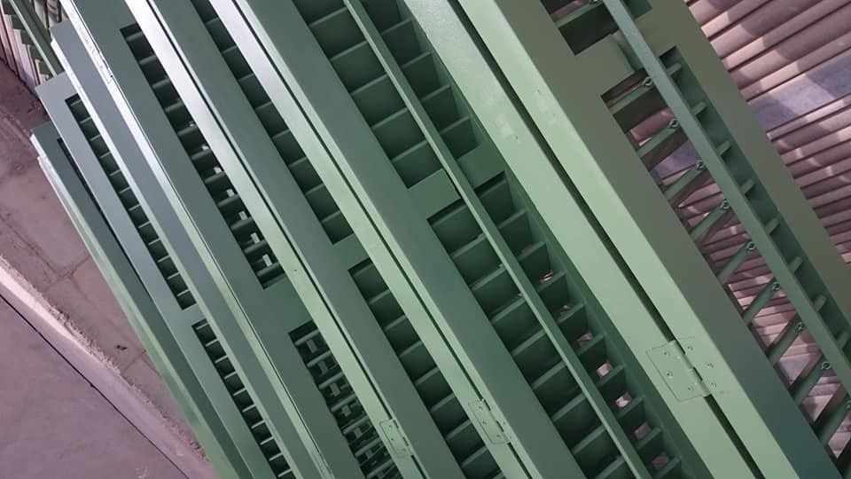 Vista diagonal de barandillas o contraventanas de metal verde contra una pared rosa.