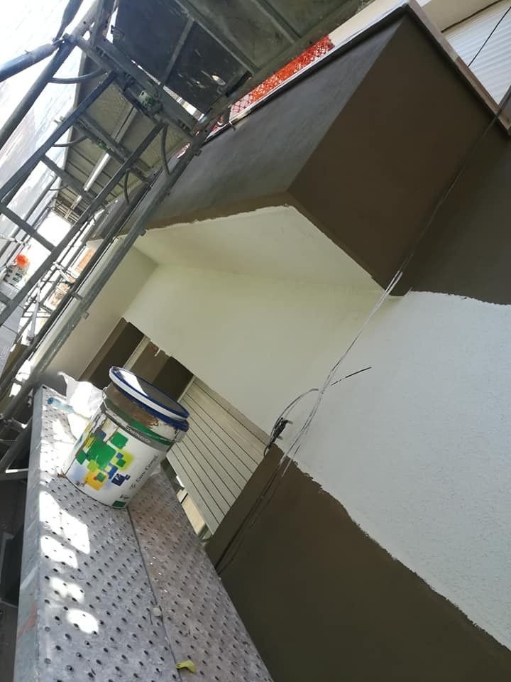 Pasarela exterior cubierta con paredes marrones y blancas, andamios metálicos y un pequeño cubo en el suelo.