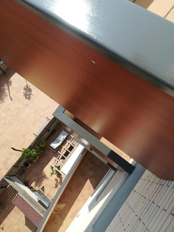 Vista rotada del patio de un edificio con una pasarela, una pared naranja y el borde del tejado gris.