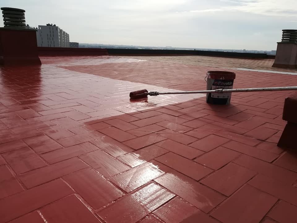 Terraza roja en la azotea con baldosas de ladrillo mojadas y una fregona o un palo tirado en el suelo cerca del borde.