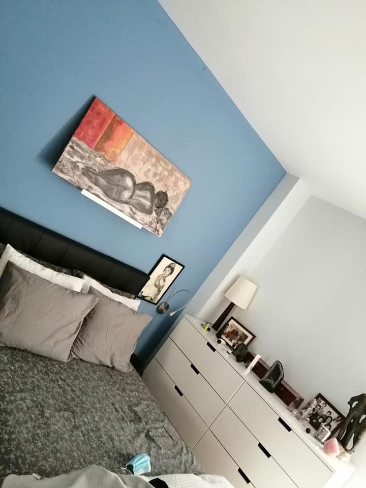 Vista inclinada de un dormitorio con una pared decorativa azul, cama, cómoda
