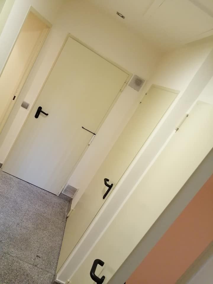 Pasillo inclinado con varias puertas blancas y manijas negras en un corredor interior de color beige.