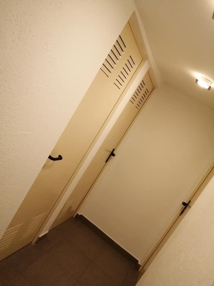 Pasillo inclinado con puertas beige, una rejilla de ventilación en la pared y una 