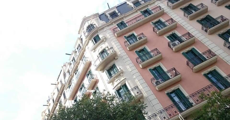 Edificio de apartamentos rosa con ventanas de contraventanas verdes visto desde un ángulo bajo contra el cielo.