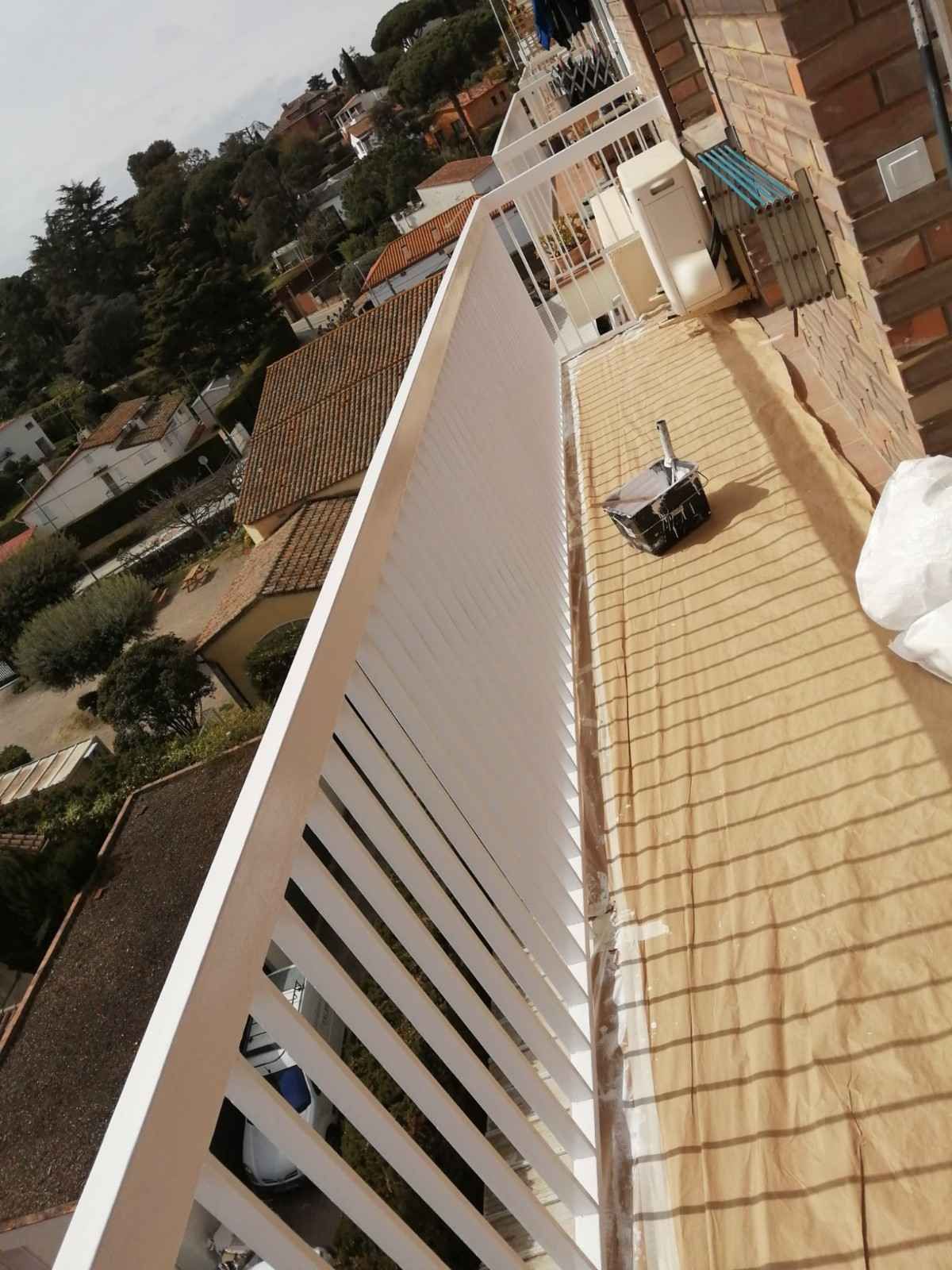 Terraza en la azotea con baldosas beige, barandilla blanca y un pequeño dispositivo con ruedas cerca de la pared.