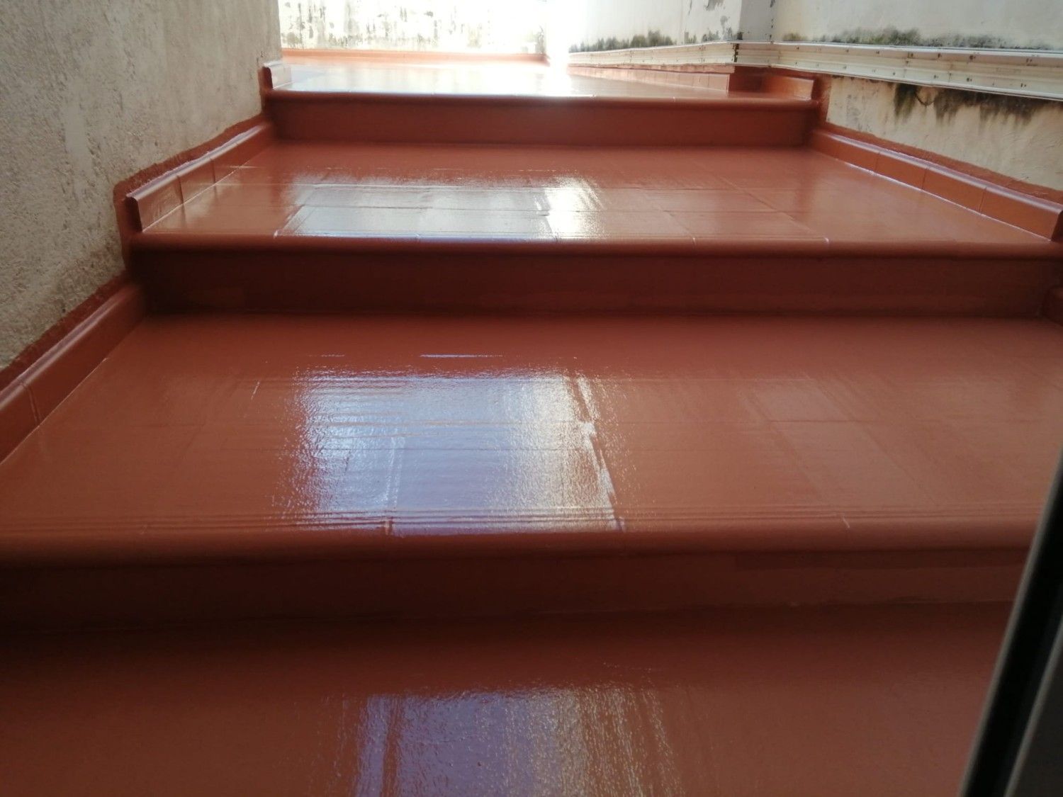 Escalera pintada de rojo brillante con escalones estrechos y una ventana luminosa en la parte superior.