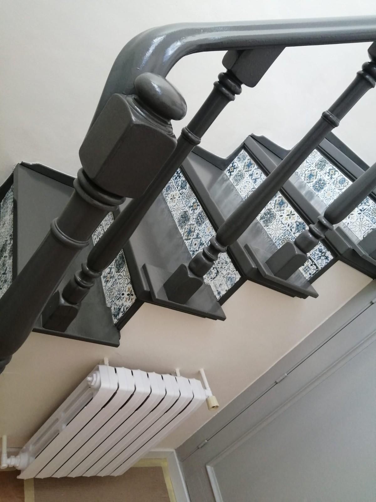 Escalera interior con barandilla gris y radiador de pared blanco, vista desde abajo.
