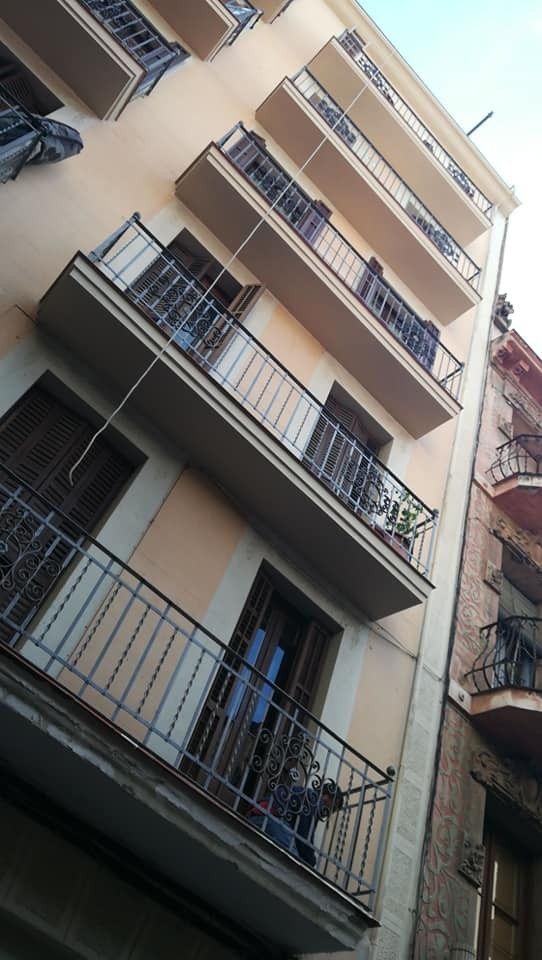 Vista inclinada de un edificio de apartamentos beige con balcones y barandillas de metal contra el cielo.