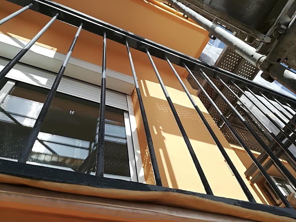 Mirando hacia arriba la fachada naranja del edificio y las barandillas de metal negro desde abajo.