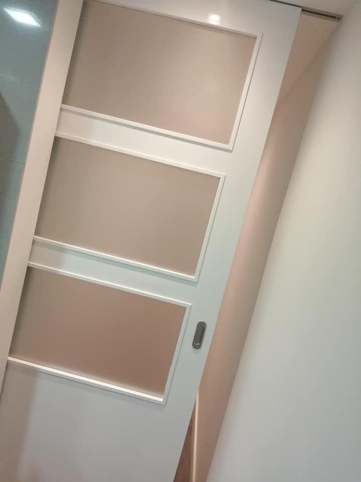 Vista inclinada de una puerta blanca con tres paneles de vidrio esmerilado y una manija plateada en un pasillo.