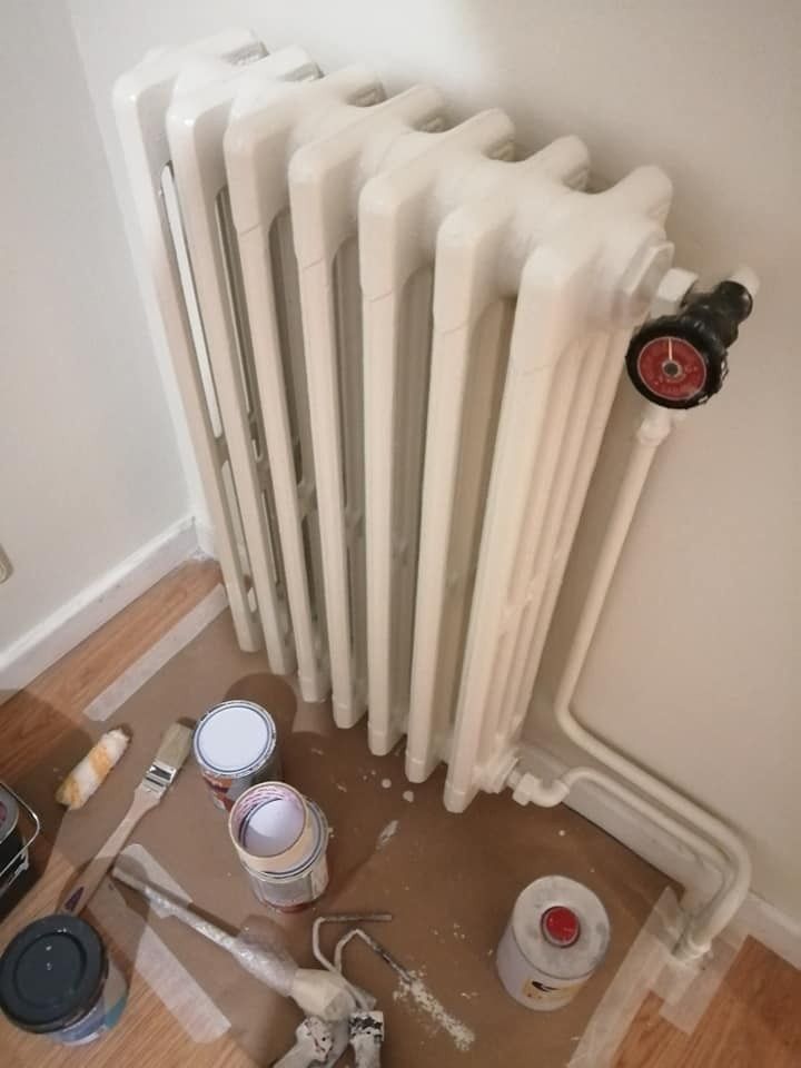 Radiador blanco con válvulas y materiales de pintura en el suelo