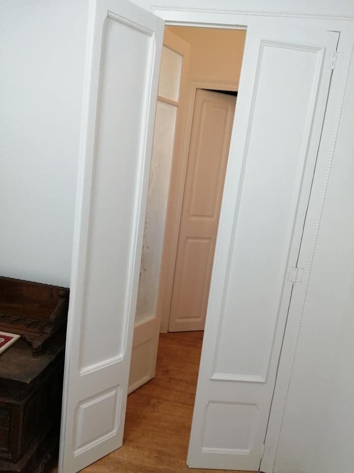 Se abren unas puertas dobles blancas que dan a un pasillo de color beige con una puerta cerrada al otro lado.