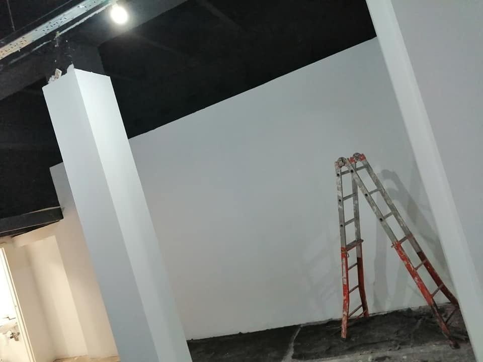 Dos escaleras apoyadas contra una pared blanca en una zona de construcción al aire libre, en penumbra, por la noche.