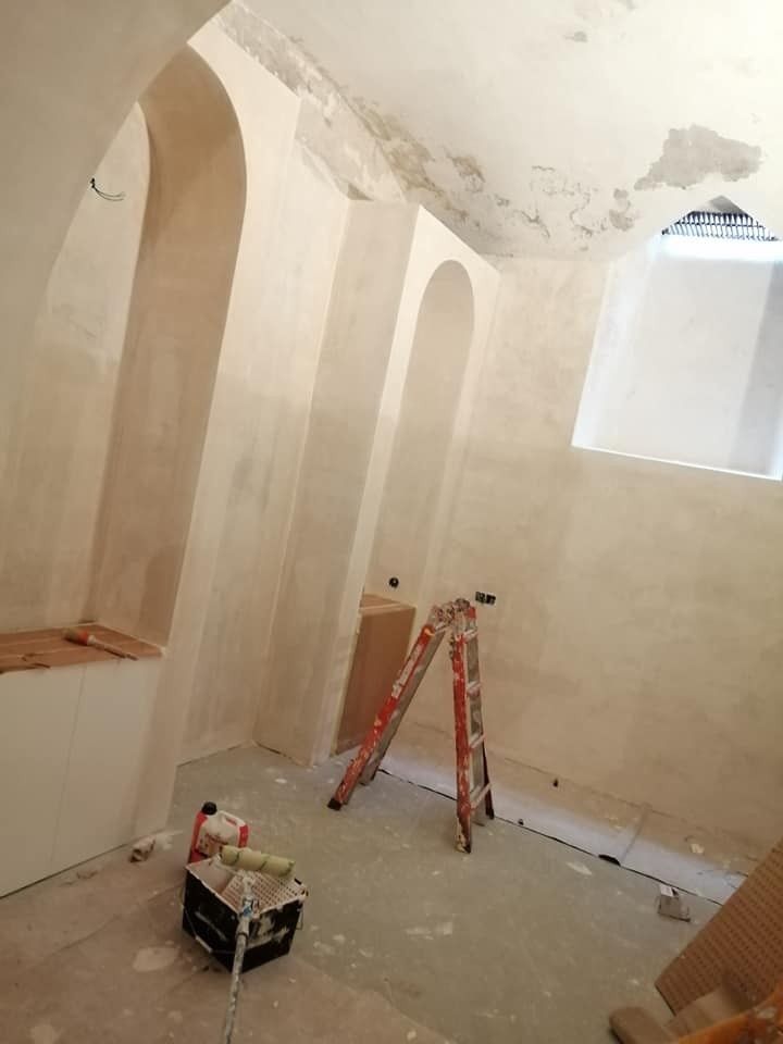 Habitación pequeña en proceso de renovación con escalera, materiales de pintura y paredes y techo sin terminar.