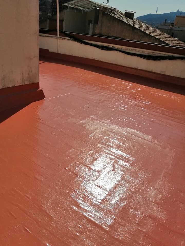 Terraza roja impermeable en la azotea, junto a un muro, con las azoteas vecinas al fondo.