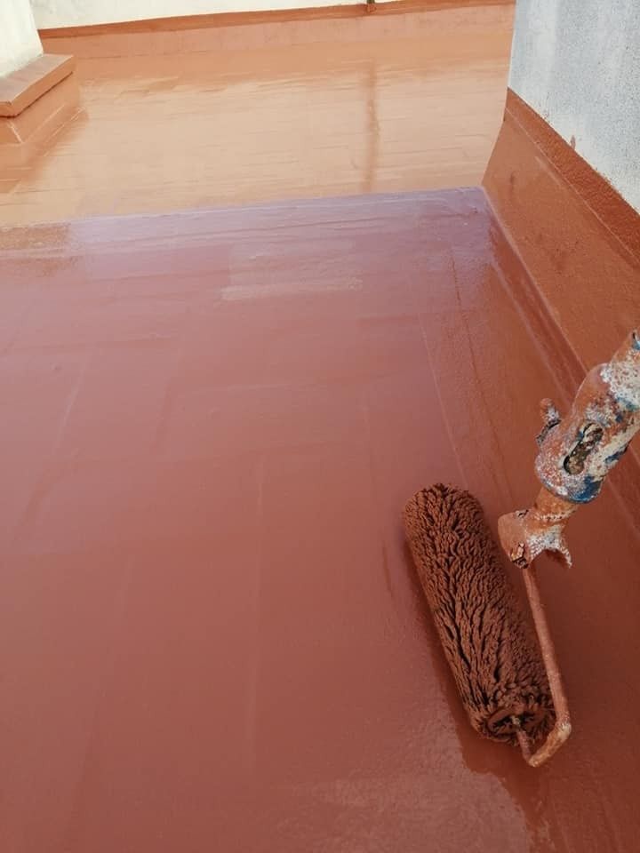 Un suelo húmedo de color marrón rojizo que está siendo fregado con una fregona de cuerdas cerca de una pared y una puerta.