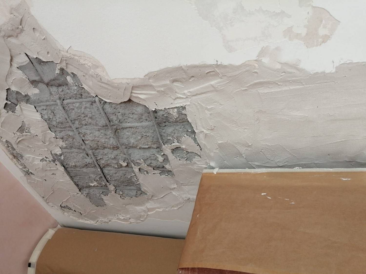 Pared dañada con yeso descascarado y una mancha gris expuesta encima de una caja de cartón.