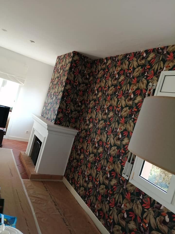 Sala de estar con papel tapiz floral, chimenea blanca y persiana inclinada.