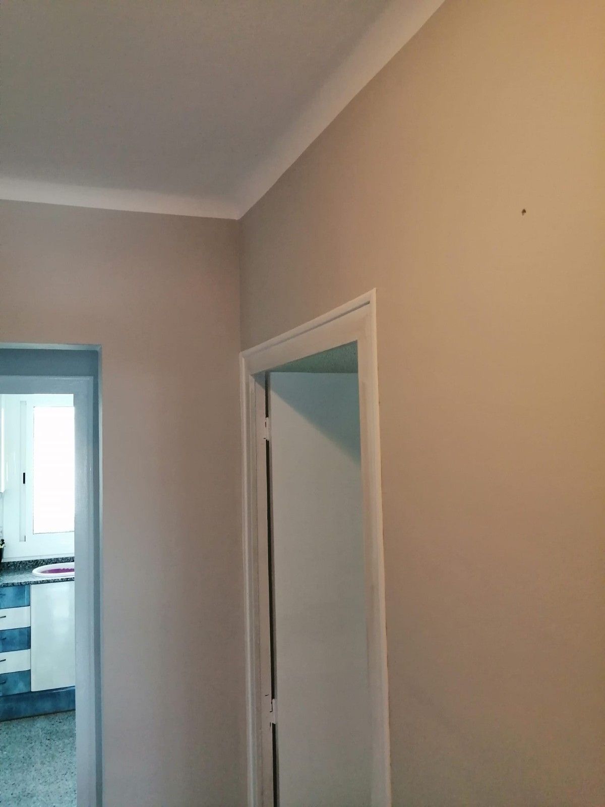 Pasillo con paredes de color beige y una puerta abierta que da a una habitación con azulejos azules, probablemente un baño.