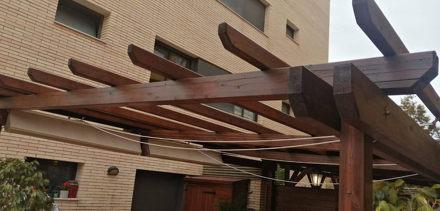 Estructura de pérgola de madera con vigas sobre un patio de ladrillo.
