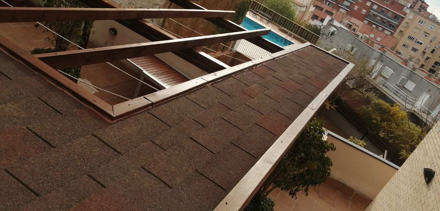 Azotea con tragaluces abiertos y tejas marrones, con vistas a edificios de apartamentos y árboles.