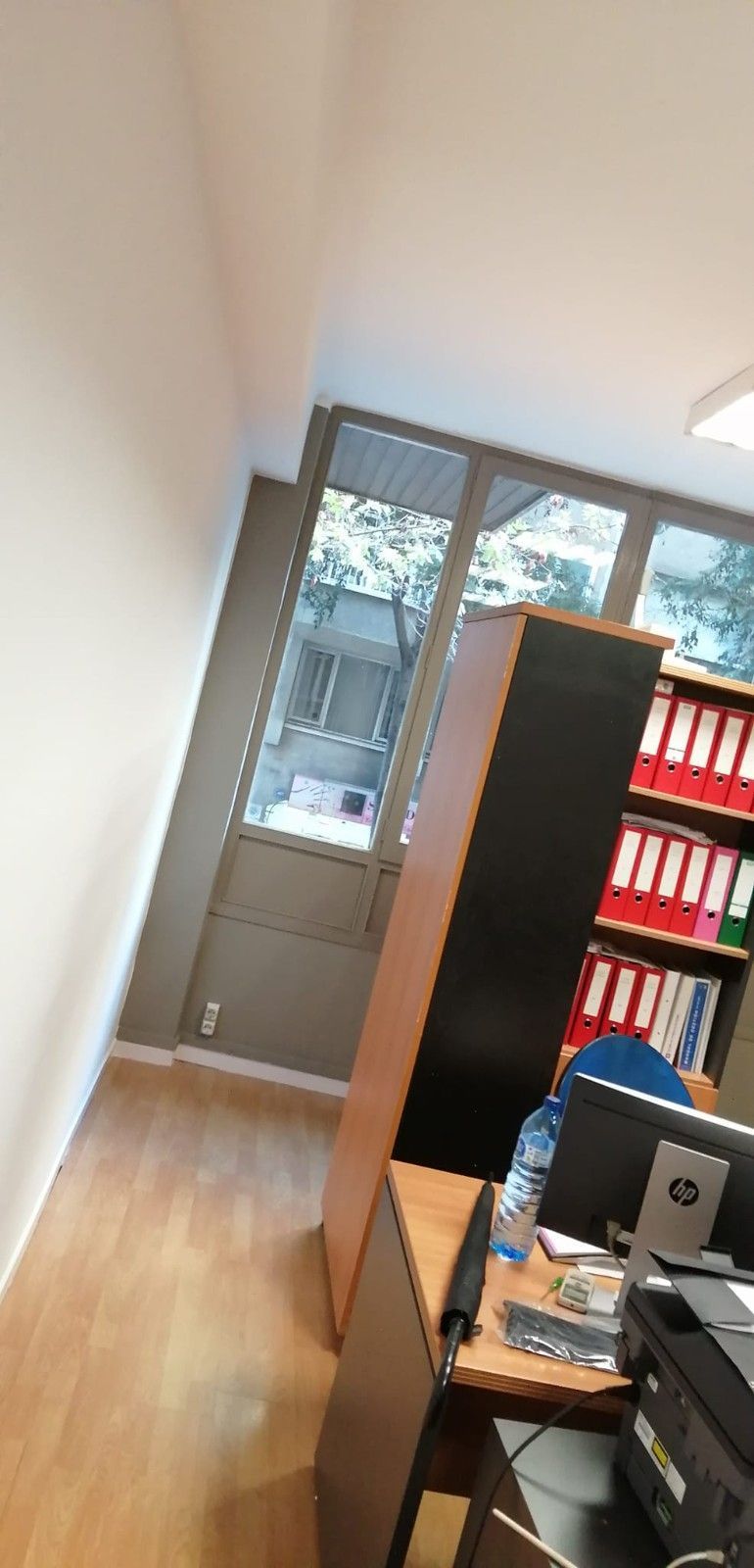 Interior de oficina inclinado con escritorio, ordenador, estantería y luz de ventana.