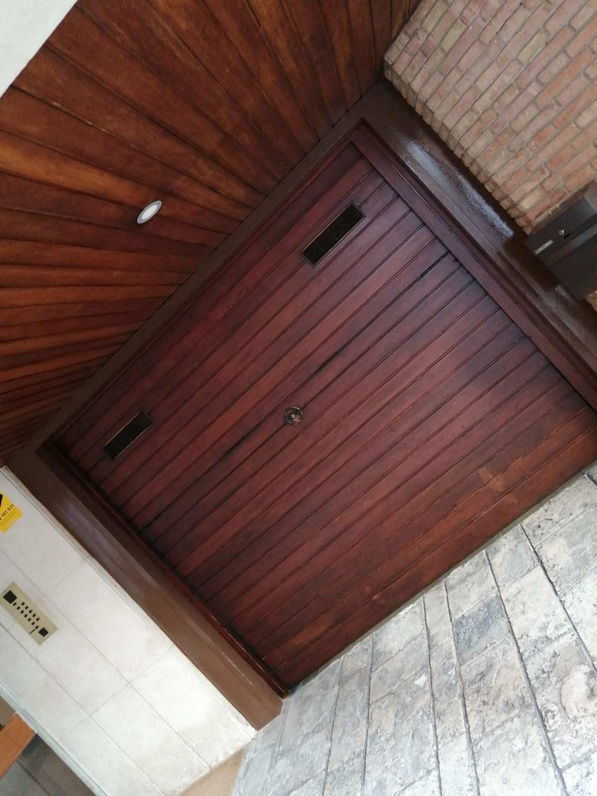 Puerta de garaje cerrada de madera de color rojo oscuro junto a paredes de ladrillo y piedra bajo un techo de madera.