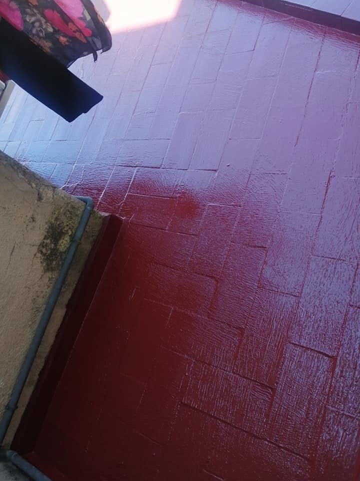 Pared y suelo pintados de rojo y mojados, junto a una pared beige y un alero oscuro.