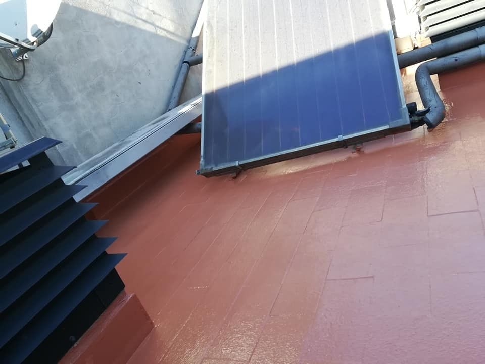 Azotea con paneles solares, techo rojo y tuberías sobre paredes grises.