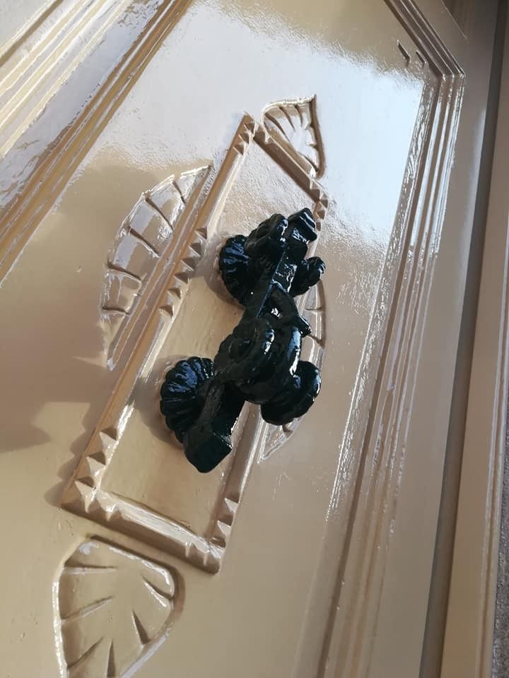 Aldaba negra ornamentada sobre una puerta con paneles beige.