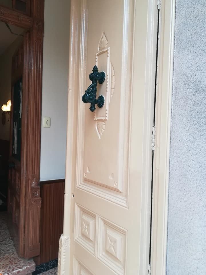 Una puerta blanca abierta con una corona oscura colgando en un pasillo.