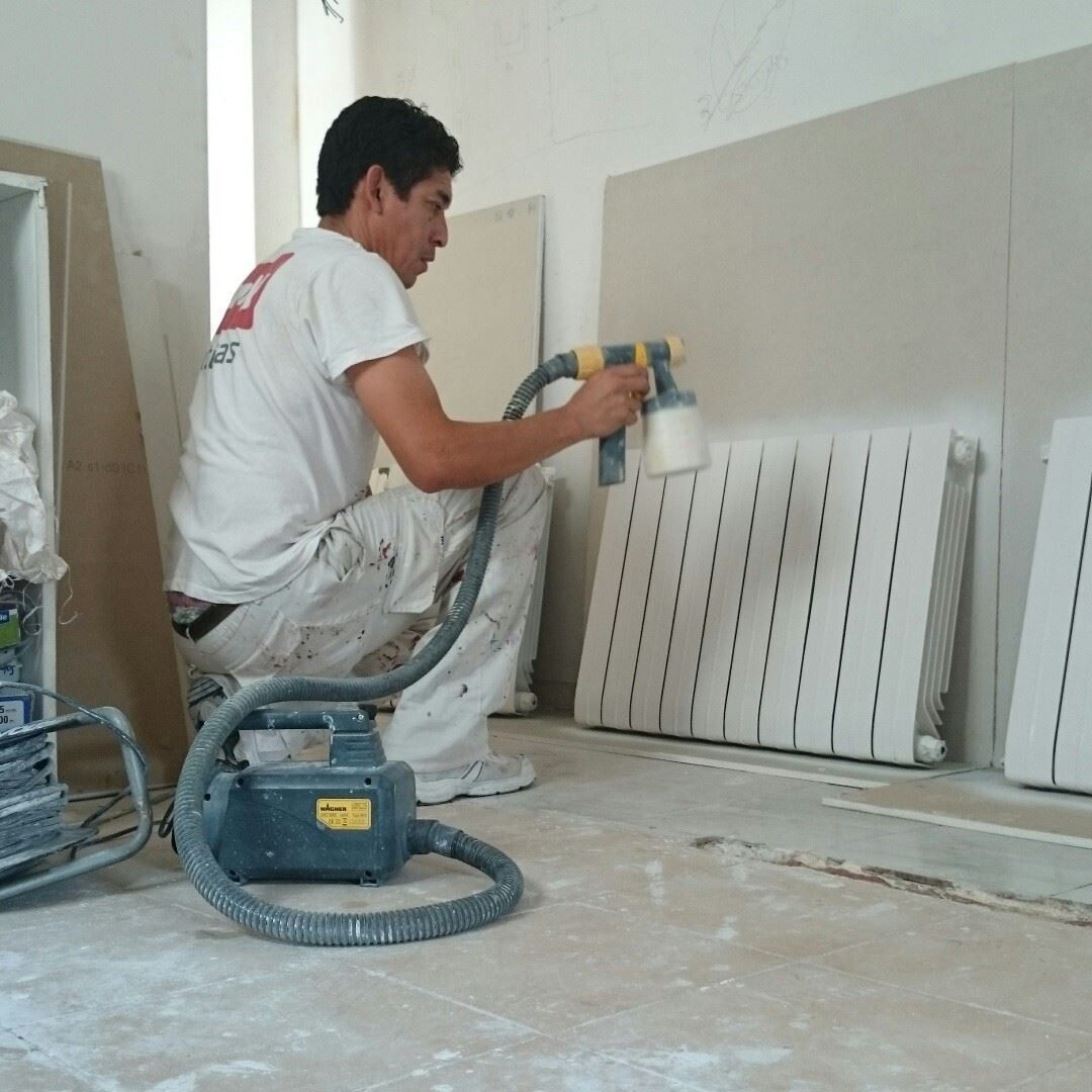 Un trabajador utiliza una pistola pulverizadora para pintar paneles de pared blancos en una habitación en obras.
