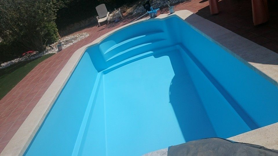 Piscina azul vacía con escalones, vista desde un ángulo junto a un patio y vegetación.