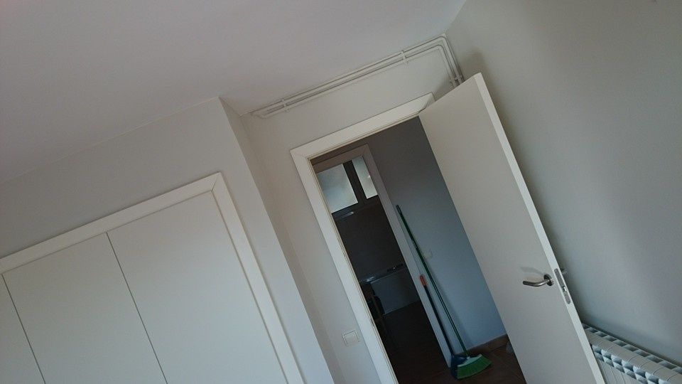 Vista inclinada de un dormitorio blanco con puertas de armario, una puerta abierta y un radiador a lo largo de la pared.