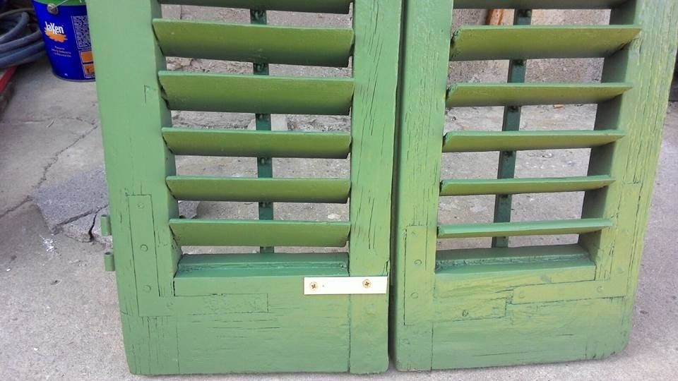 Puertas dobles de madera verde con contraventanas y pestillo cerca de la parte inferior.